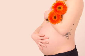 Fotografía en estudio de Lorena embarazada con tonos narajas y gerbera naranja